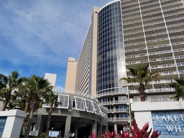 A modern hotel with a curved facade, multiple balconies, and palm trees in the foreground.