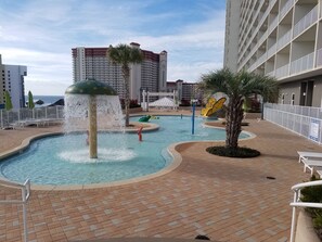 A swimming pool with a water fountain, surrounded by lounge chairs and palm trees.