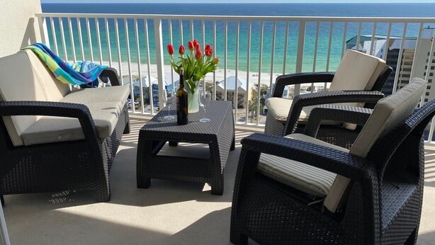 A balcony with wicker furniture, a table, and a vase of red flowers. -  Fantastic Gulfview condo 1 br/2 ba , bunk , sleep 6 (Panama City Beach)