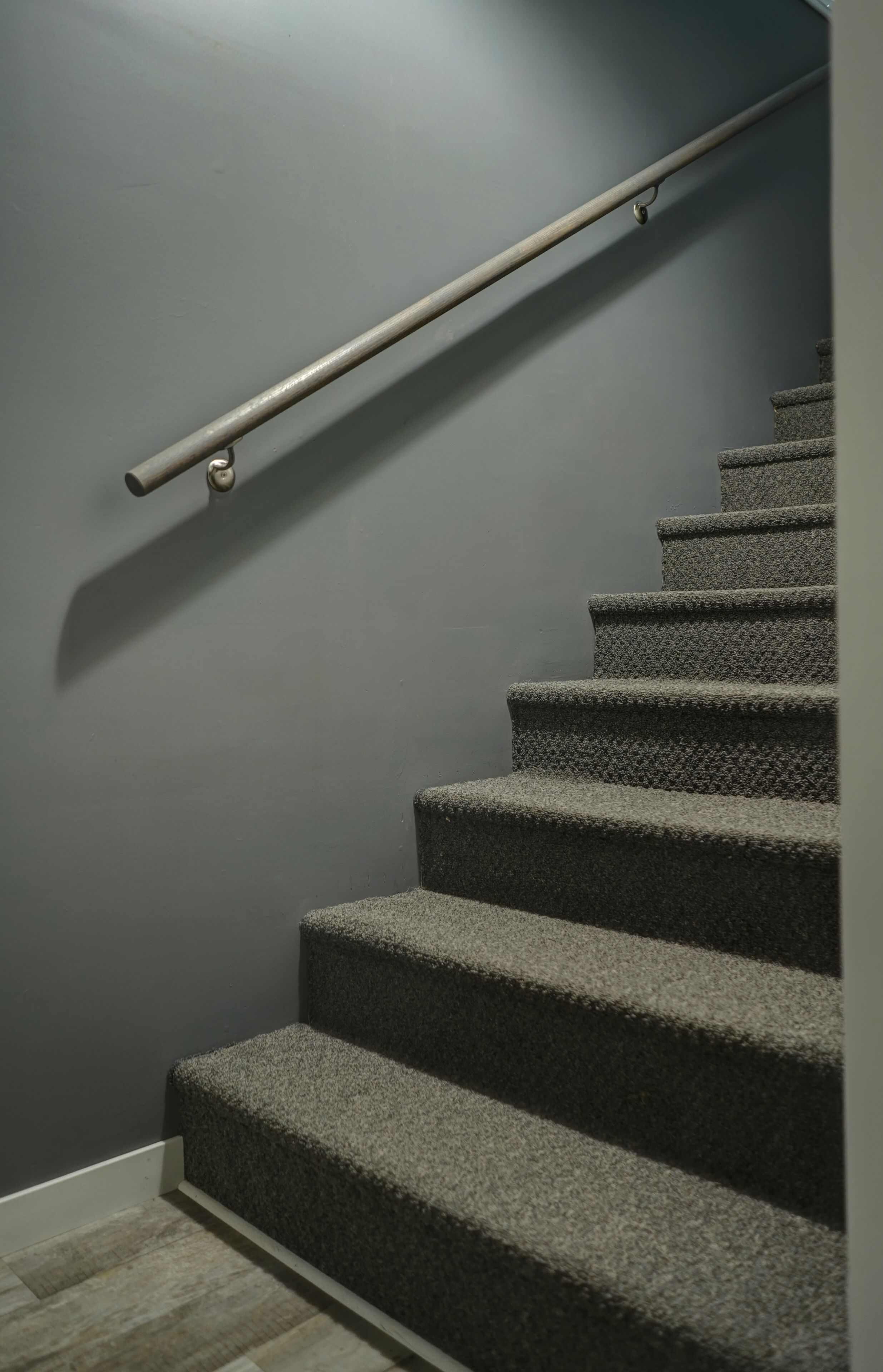 A staircase with carpeted steps and a metal handrail against a plain wall.