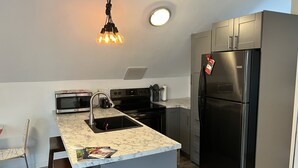 Une cuisine moderne dotée d’un îlot central intégré, d’appareils électroménagers en acier inoxydable et d’un luminaire suspendu.