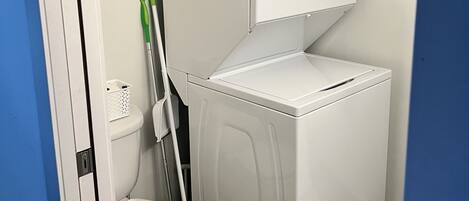 A compact laundry room with a front-loading washer and dryer stacked above a toilet.