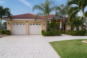 A two-story house with a red-tiled roof, two garage doors, and a paved driveway. -  WATER VIEW, DIRECT GULF ACCESS , OVERSIZE POOL, GrilL, POOL BAR , TV (Cape Coral)
