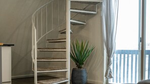 A spiral staircase with a white railing, a potted plant, and a large window with curtains. - Stylish A-Frame (Eden)