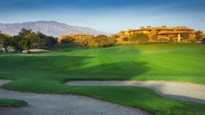 A golf course with bunkers and a building with multiple stories in the background.