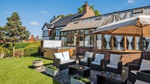 Ein Haus mit Wintergarten, Sitzgelegenheit im Freien mit Korbmöbeln und einem gepflegten Garten.