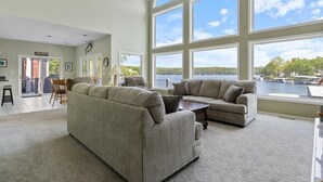 Amplio salón con grandes ventanales con vistas a un lago, con dos sofás y una mesa de centro.