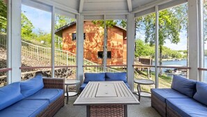 Un espacio al aire libre cubierto con sofás de mimbre y una mesa central, con vista a un lago y una cabaña de madera.