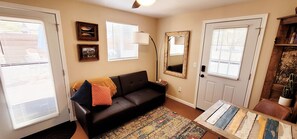 A living room with a black leather sofa, a patterned rug, a wooden coffee table, and a cactus on a wooden shelf.