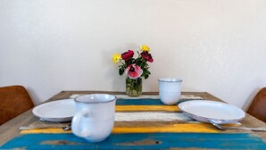 Una mesa de comedor con un jarrón de flores, dos tazas blancas y una cuchara.