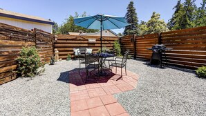 Un área de patio con una mesa y sillas, una parrilla y una valla de madera.