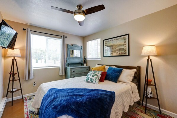A bedroom with a bed, ceiling fan, bedside lamps, a dresser, and a window with curtains.