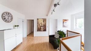 A modern kitchen with a wooden floor, white cabinetry, a wall clock, and a large cityscape painting. - P1 - Large apartment at the gates of Kassel (Fuldatal)