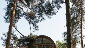 A two-story house with a curved roof, a front porch, and a well-maintained lawn.