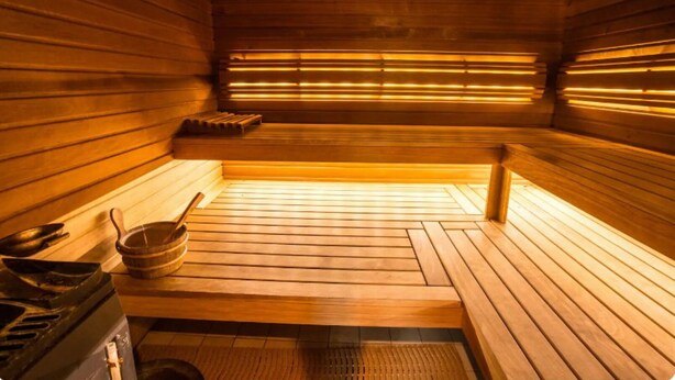A sauna with wooden benches and a bench in the center. There are two bowls and a ladle on the floor.