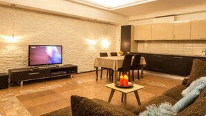 A modern living room with a flat-screen TV, a dining table, and a kitchen area with cabinets and a countertop.