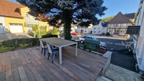 A wooden deck with a table and chairs, surrounded by greenery and a large tree. - P4 - Large apartment at the gates of Kassel (Simmershausen)