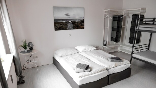 A modern bedroom with a large bed, a bedside table with a lamp, a small potted plant, a wall-mounted picture, and a bunk bed structure. - P4 - Large apartment at the gates of Kassel (Simmershausen)