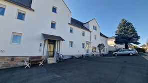A white building with multiple windows and a door, a parked car, and a large tree. - P4 - Large apartment at the gates of Kassel (Simmershausen)