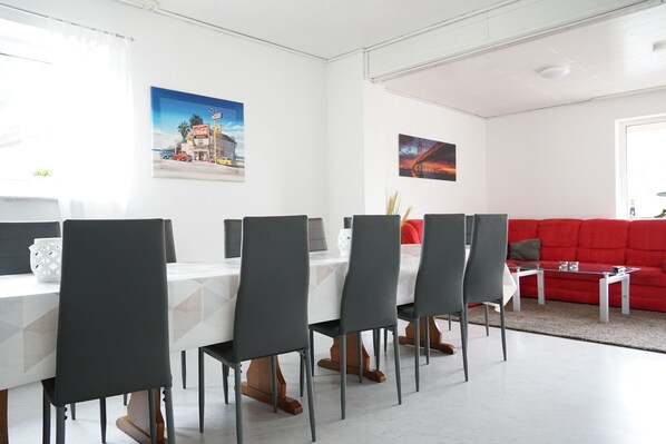 Un espace repas moderne avec une table blanche et des chaises noires, un canapé rouge et deux œuvres d’art murales.