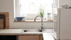 A kitchen with a stainless steel sink, a window with a view of a white building, a wooden cutting board, and a white refrigerator. - P4 - Large apartment at the gates of Kassel (Simmershausen)