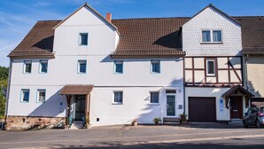 A two-story house with a brown tiled roof, a front entrance with steps, and a garage door. - P4 - Large apartment at the gates of Kassel (Simmershausen)