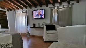 A hotel room with a bed, a sofa, a TV mounted on the wall, and a small shelf with decorative items. - True "Village Refuge" in Monsaraz (pets allowed!)  (Monsaraz)