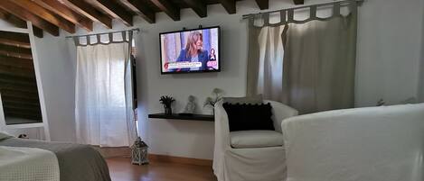 A hotel room with a bed, a sofa, a TV mounted on the wall, and a small shelf with decorative items.