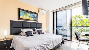 Une chambre moderne avec un grand lit, un tableau au-dessus du lit et une porte-fenêtre coulissante donnant sur un balcon.