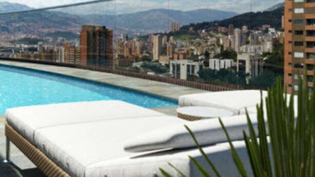 Une piscine sur le toit, agrémentée de chaises longues, offrant une vue dégagée sur le paysage urbain et, au loin, sur une chaîne de montagnes.