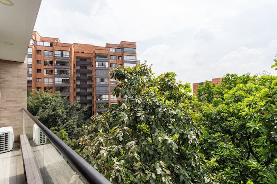 Un balcone con vista su un edificio a più piani e vegetazione lussureggiante.