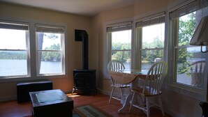 Una habitación con ventanas amplias que dan a un lago, una chimenea, una mesa de comedor con sillas y una alfombra.