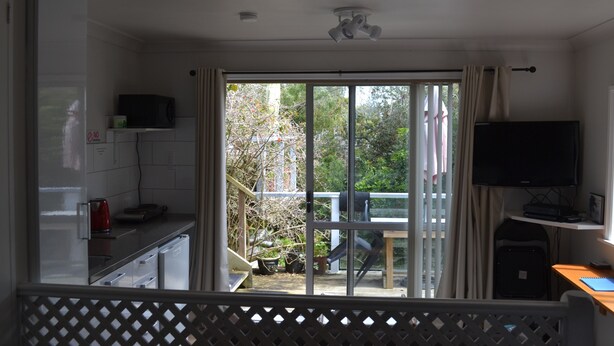 A room with a kitchen area, a dining table, a TV, and a sliding glass door leading to an outdoor area. - The Lighthouse (Torbay)