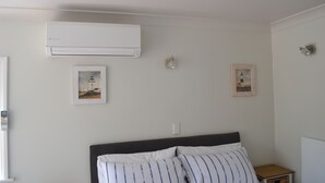 A bedroom with a bed, an air conditioner, two framed pictures, a bedside lamp, and a small wooden nightstand. - The Lighthouse (Torbay)