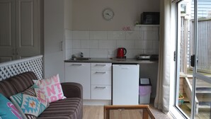 A compact kitchen with white cabinets, a refrigerator, a microwave, and a clock on the wall. - The Lighthouse (Torbay)