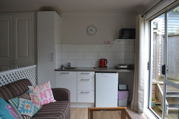 A compact kitchen with white cabinets, a refrigerator, a microwave, and a clock on the wall. - The Lighthouse (Torbay)
