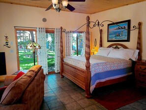 A bedroom with a four-poster bed, a wooden ceiling fan, a large window with curtains, and a painting on the wall. - The Crestone Casitas: Casita Suite #1 (Saguache County)