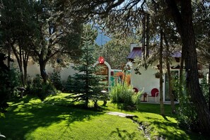A garden with a lawn, trees, and a building with a red roof. - The Crestone Casitas: Casita Suite #1 (Saguache County)