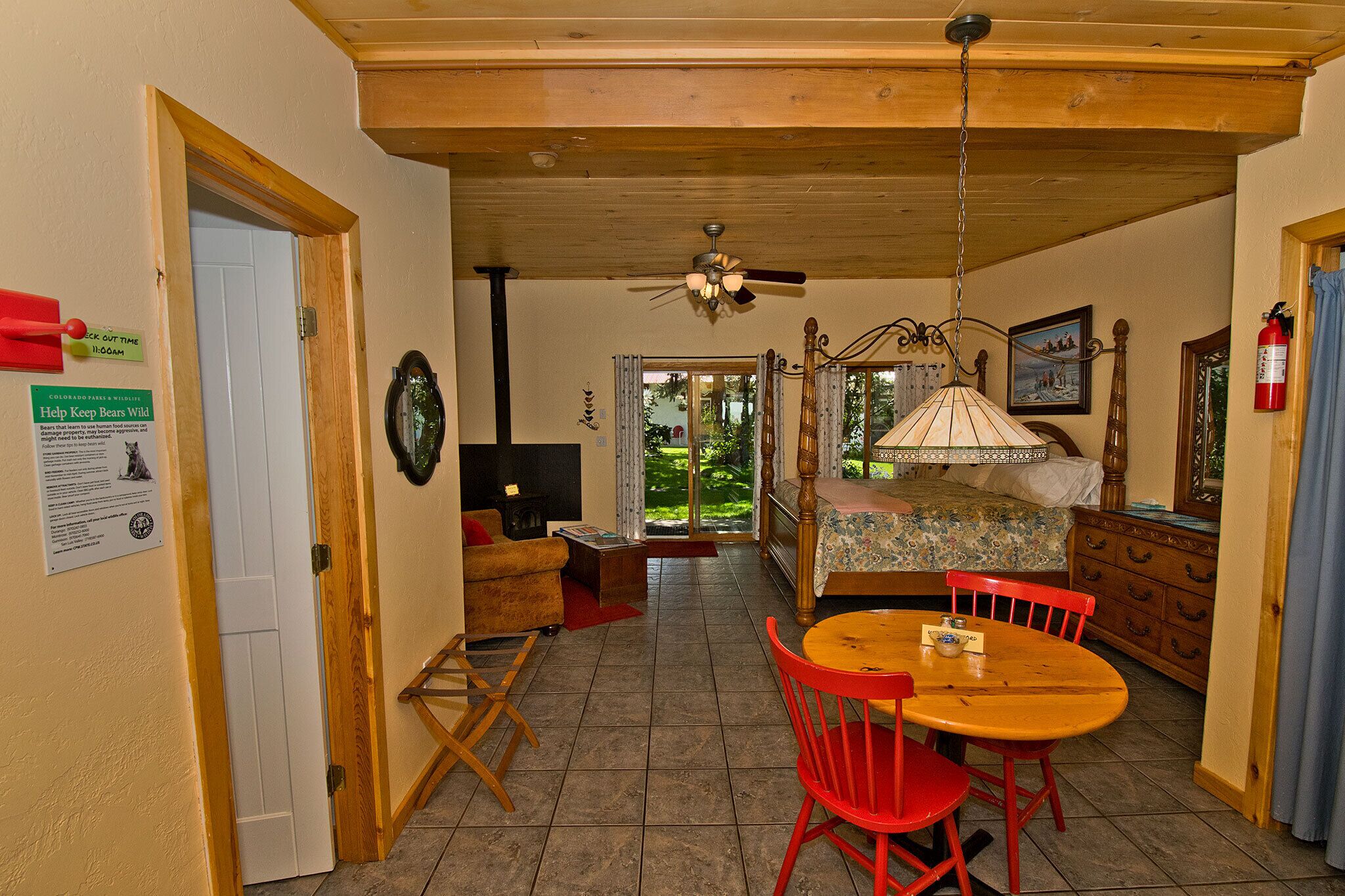 A room with a bed, a dining table with chairs, a ceiling fan, and a fireplace.