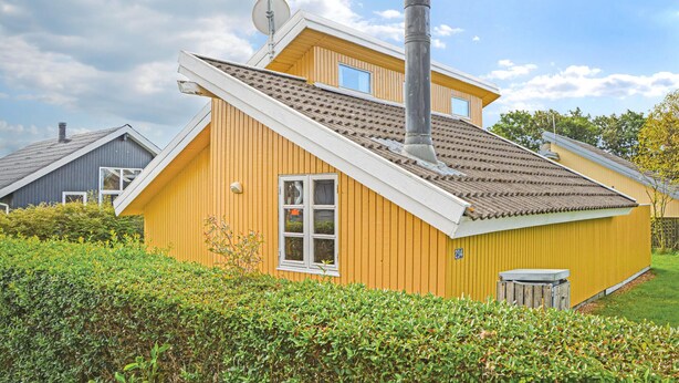 Une maison jaune avec un toit en pente, une cheminée et une petite fenêtre.