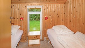 Une pièce aux murs lambrissés, comprenant deux lits, une fenêtre et une petite table en bois.