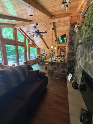 A wooden interior with a stone fireplace, a wooden ceiling, and large windows.