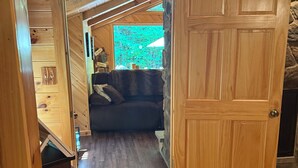 A wooden interior with a couch, a door, and a window with a view. - Beautiful 2 BR cabin with a wall of windows overlooking the deck and stream. (Dayton)