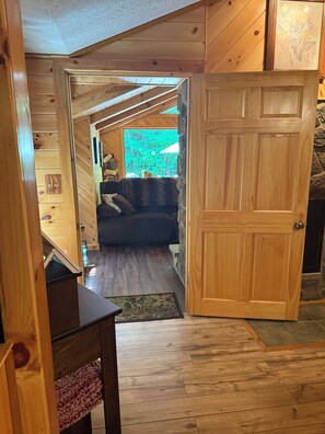 A wooden interior with a couch, a door, and a window with a view.