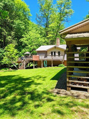 Eine rustikale Holzhütte mit einer Holzdielen-Terrasse, einem Steinkamin und einem grünen Rasen.