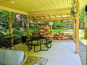 Eine überdachte Terrasse mit Tisch und Bänken, umgeben von einem Holzzaun und Pflanzen.