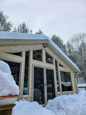 Una casa con ventanas amplias, techo inclinado y acumulación de nieve alrededor de los cimientos.