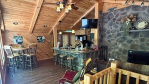 A wooden interior with a dining area, bar, and stone fireplace. - Beautiful 2 BR cabin with a wall of windows overlooking the deck and stream. (Dayton)