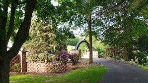 A paved driveway leading to a gated entrance with a stone wall and a decorative archway. - Romantic hideaway on the lake nestled in the pines 79 miles north of Pittsburgh. (Ringgold)