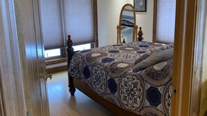 A bedroom with a bed, wooden headboard, ceiling fan, and large windows with blinds. - Romantic hideaway on the lake nestled in the pines 79 miles north of Pittsburgh. (Ringgold)